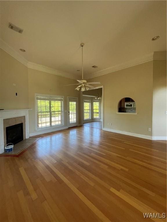 unfurnished living room with a healthy amount of sunlight, a tiled fireplace, a ceiling fan, and visible vents