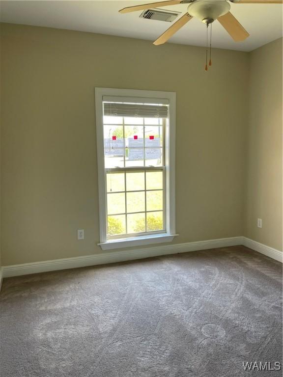 empty room with carpet floors, a ceiling fan, baseboards, and visible vents