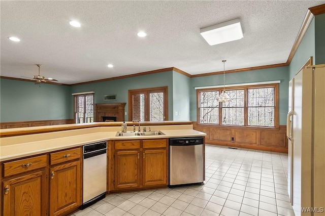kitchen with a wainscoted wall, dishwasher, brown cabinets, a sink, and freestanding refrigerator