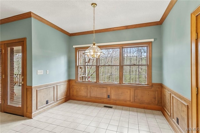unfurnished dining area featuring an inviting chandelier, a wainscoted wall, a textured ceiling, and visible vents