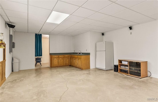 interior space featuring freestanding refrigerator, concrete floors, a sink, and a drop ceiling