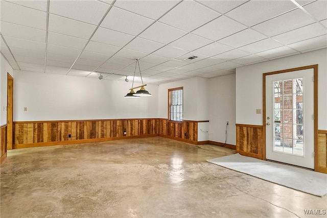 interior space with wood walls, wainscoting, finished concrete floors, visible vents, and a paneled ceiling