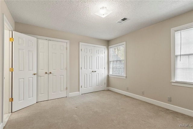 unfurnished bedroom with carpet floors, a textured ceiling, multiple closets, baseboards, and visible vents