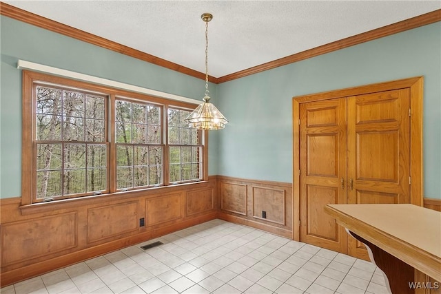 dining room with a textured ceiling, visible vents, wainscoting, ornamental molding, and a notable chandelier