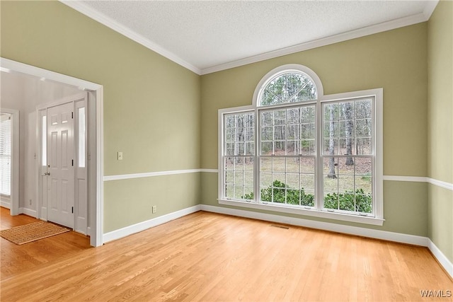empty room featuring wood finished floors, ornamental molding, a textured ceiling, and visible vents