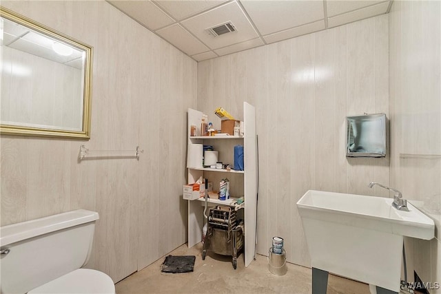 half bath with toilet, concrete floors, a sink, visible vents, and a paneled ceiling