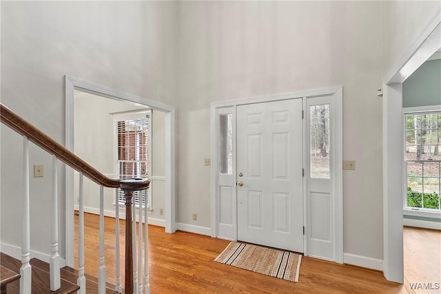 foyer entrance featuring stairs, a high ceiling, light wood-style flooring, and baseboards