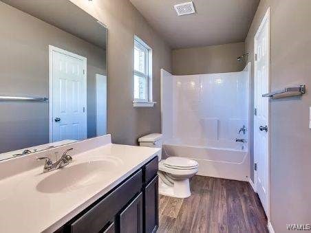 full bathroom featuring hardwood / wood-style flooring, washtub / shower combination, vanity, and toilet