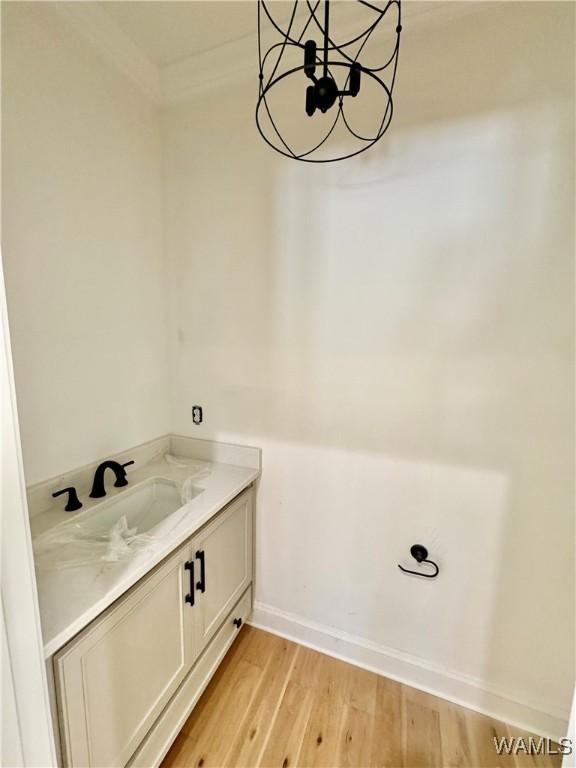 bathroom with baseboards, wood finished floors, an inviting chandelier, crown molding, and vanity