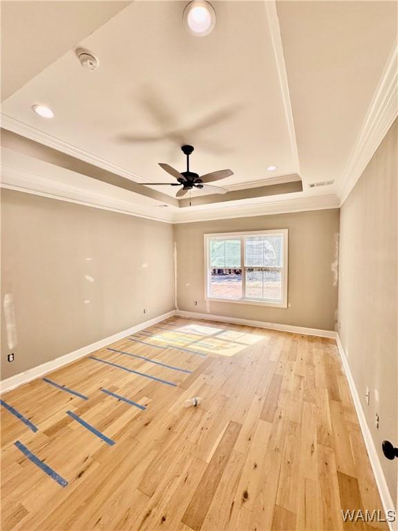 unfurnished room featuring baseboards, light wood-type flooring, a raised ceiling, and crown molding