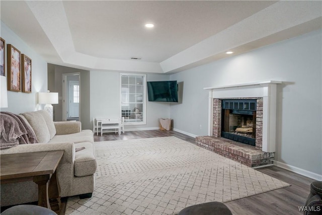 living room featuring hardwood / wood-style flooring, a tray ceiling, and a brick fireplace