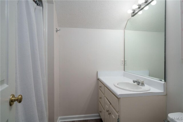 bathroom featuring lofted ceiling, vanity, a textured ceiling, toilet, and walk in shower