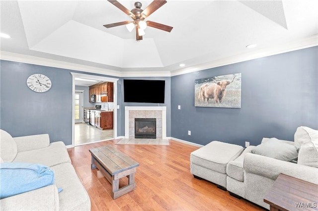 living area featuring light wood finished floors, a tile fireplace, a raised ceiling, and baseboards