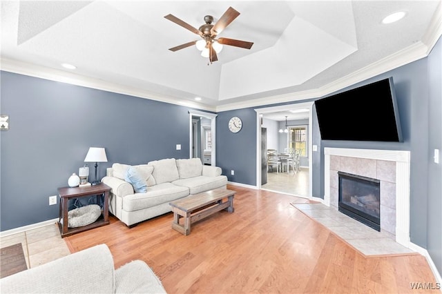 living room with a raised ceiling, ceiling fan with notable chandelier, wood finished floors, crown molding, and baseboards