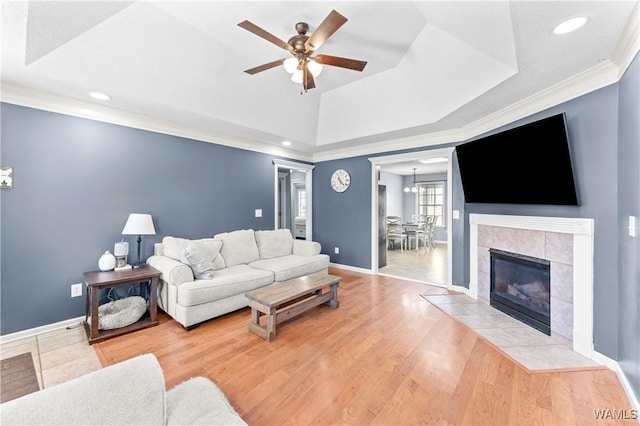 living area featuring ornamental molding, ceiling fan with notable chandelier, a tray ceiling, wood finished floors, and baseboards