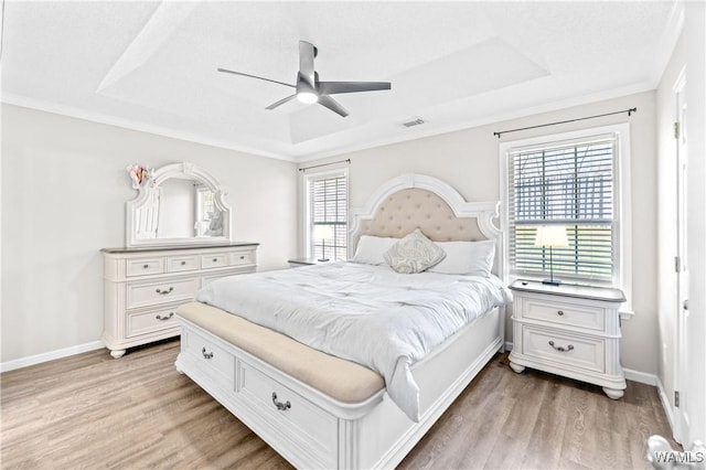 bedroom with visible vents, baseboards, a raised ceiling, and light wood-style floors