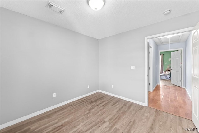 spare room with visible vents, a textured ceiling, wood finished floors, baseboards, and attic access