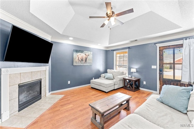 living room with baseboards, a tray ceiling, a fireplace, light wood-style floors, and a ceiling fan