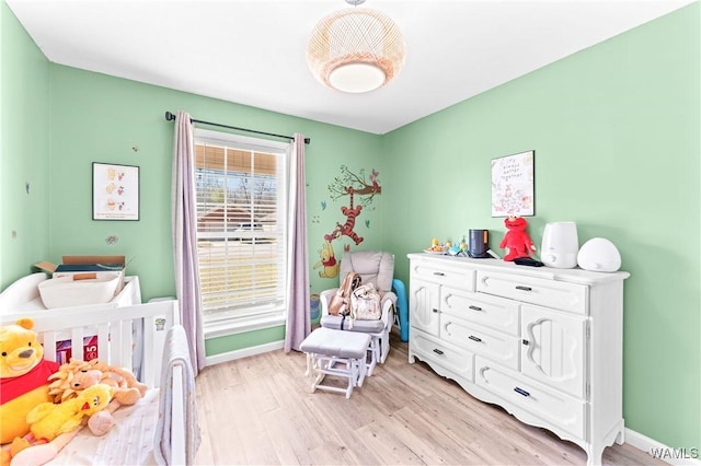 bedroom with a nursery area, baseboards, and light wood-style floors