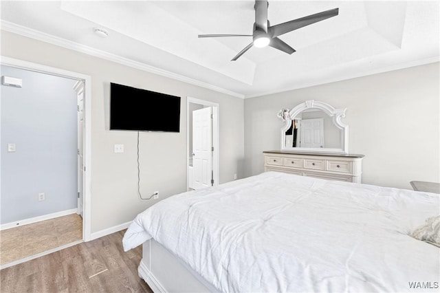 bedroom featuring a tray ceiling, baseboards, wood finished floors, and ornamental molding