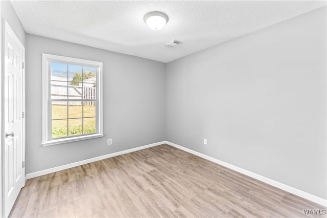 spare room with visible vents, baseboards, a textured ceiling, and wood finished floors