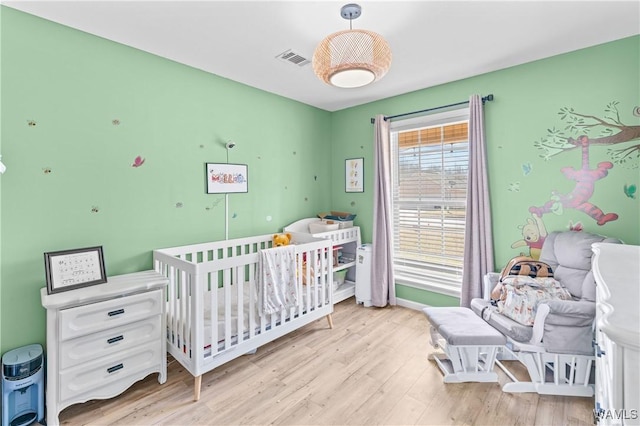 bedroom featuring light wood-style flooring, a nursery area, and visible vents