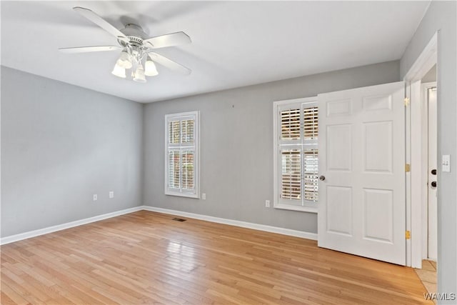 empty room featuring light wood-style floors, ceiling fan, visible vents, and baseboards