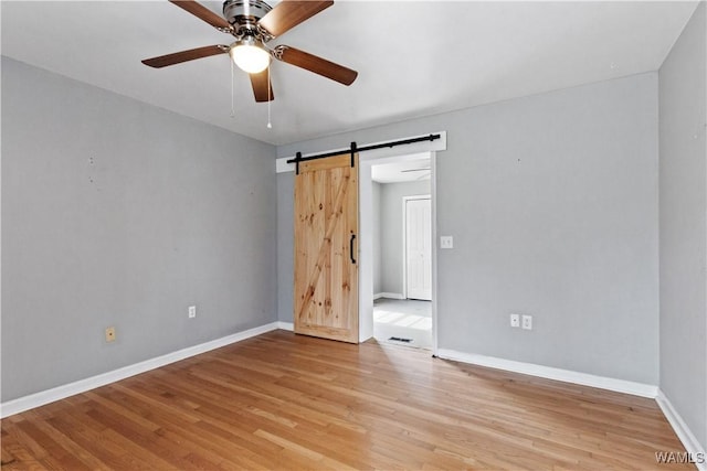 spare room featuring baseboards, a barn door, a ceiling fan, and light wood-style floors