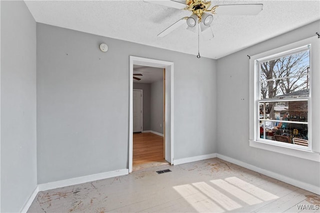 empty room featuring a textured ceiling, visible vents, a ceiling fan, and baseboards