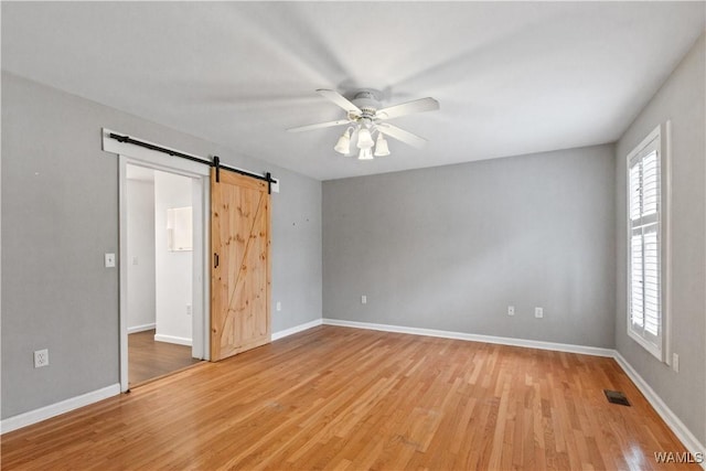 unfurnished bedroom with baseboards, a barn door, visible vents, and light wood-style floors