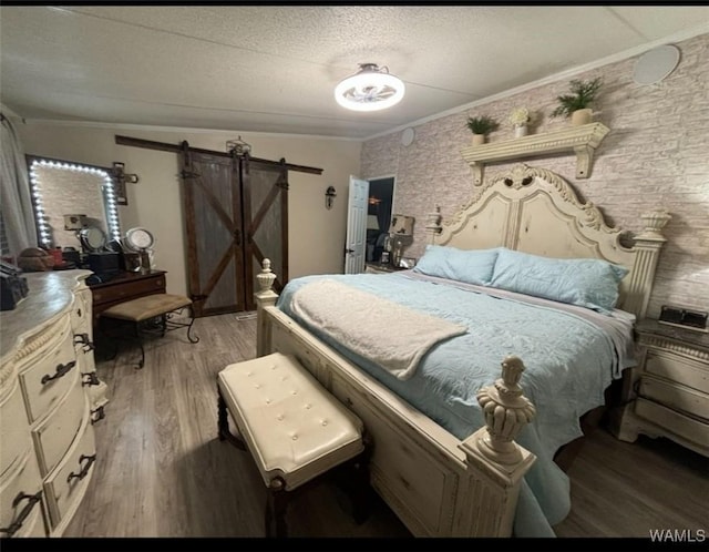 bedroom featuring a barn door, crown molding, light wood-style flooring, and a textured ceiling