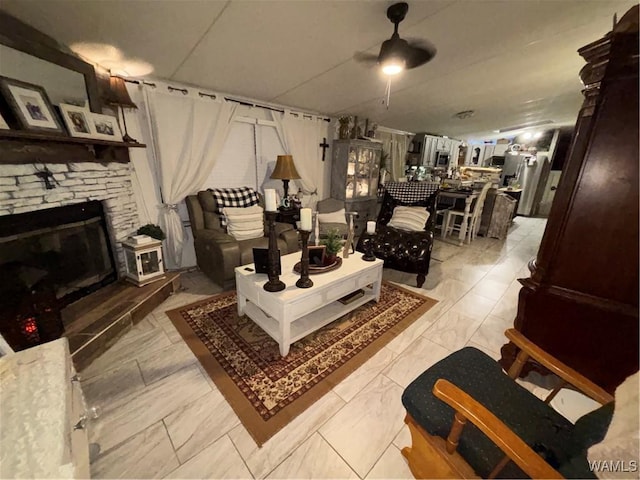 living area with ceiling fan, light marble finish flooring, and a stone fireplace