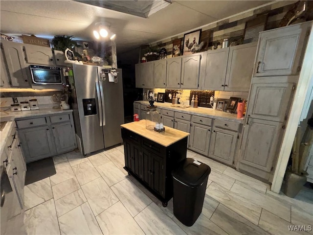 kitchen with stainless steel refrigerator with ice dispenser, light marble finish flooring, a kitchen island, decorative backsplash, and wooden counters