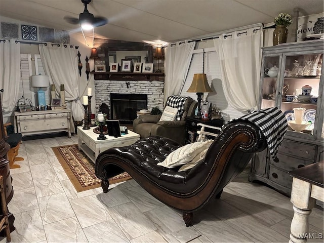 living area featuring ceiling fan, a stone fireplace, and marble finish floors