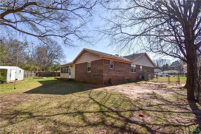 view of side of home with brick siding, fence, a lawn, a storage shed, and an outbuilding