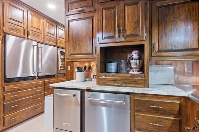 kitchen featuring stainless steel dishwasher, light tile patterned flooring, and light stone countertops