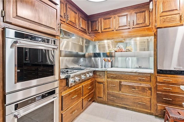 4704 Oneida Ave, Northport, AL 35473 - kitchen with appliances with stainless steel finishes, light tile patterned floors, brown cabinetry, tasteful backsplash, and light stone countertops