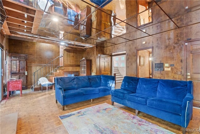 living room featuring a towering ceiling, wooden walls, and stairway