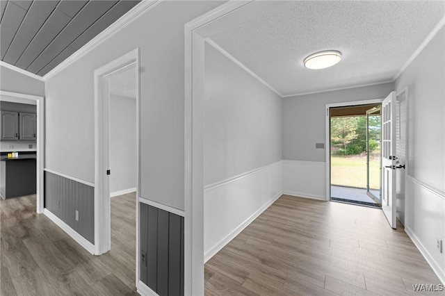 corridor featuring wood finished floors, a textured ceiling, and ornamental molding