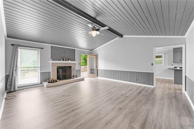 unfurnished living room featuring vaulted ceiling with beams, wooden ceiling, light wood-style floors, wainscoting, and a brick fireplace