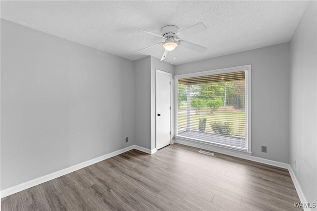 unfurnished room with a textured ceiling, wood finished floors, visible vents, and ceiling fan