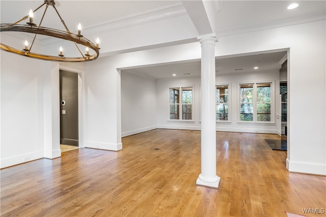 unfurnished room featuring light wood-type flooring, decorative columns, an inviting chandelier, and crown molding