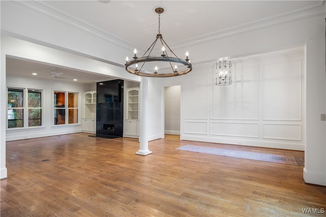 unfurnished living room with hardwood / wood-style flooring, ceiling fan with notable chandelier, ornate columns, and crown molding