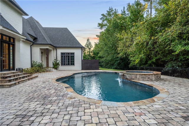 pool at dusk featuring pool water feature, an in ground hot tub, and a patio