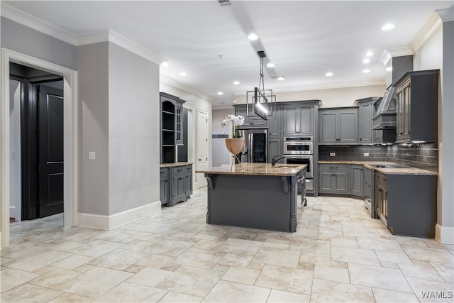 kitchen with gray cabinetry, backsplash, a center island with sink, crown molding, and light stone counters