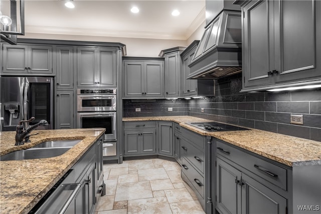 kitchen featuring decorative backsplash, appliances with stainless steel finishes, light stone counters, custom exhaust hood, and sink