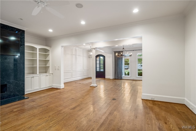 unfurnished living room featuring ceiling fan with notable chandelier, light wood-type flooring, ornamental molding, and decorative columns