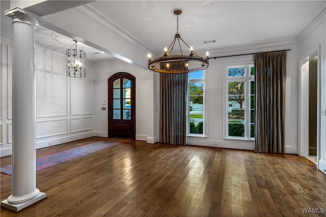 unfurnished dining area featuring ornate columns, crown molding, dark wood-type flooring, and a notable chandelier