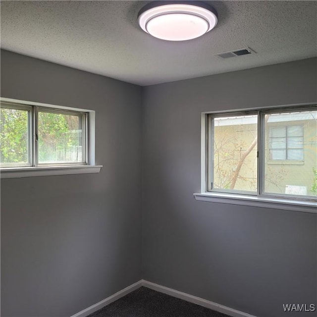 spare room featuring plenty of natural light, baseboards, visible vents, and a textured ceiling