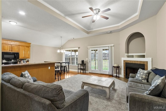 living area with a raised ceiling, ceiling fan with notable chandelier, wood finished floors, and a tile fireplace